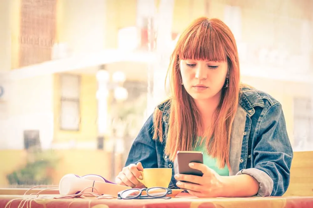 Ein rothaariges Mädchen sitzt in einem Café und benutzt ein Handy
