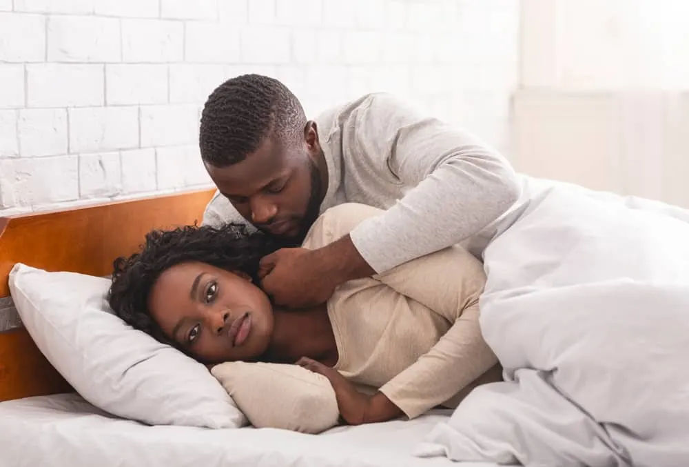 Ein schwarzer Mann in einem Schlafzimmerbett streichelt das Gesicht einer wütenden Frau