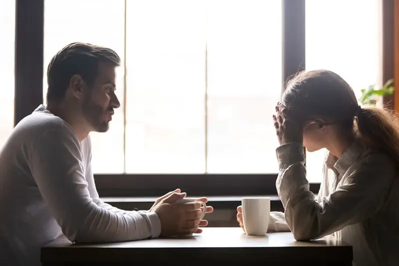 Eine Frau berührt ihre Stirn, während ein Mann im Café mit ihr spricht