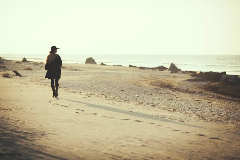 Eine Frau mit Mantel setzt den Strand