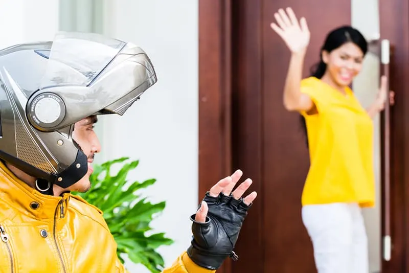 Eine Frau, die an der Tür steht und ihrem Freund mit Helm winkt