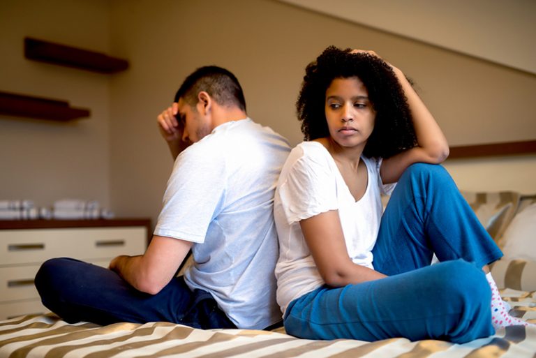 eine besorgte Frau, die neben einem depressiven Mann auf dem Bett sitzt