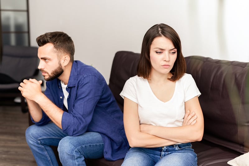 Eine frustrierte Frau mit verschränkten Armen sitzt neben ihrem Freund auf der Couch