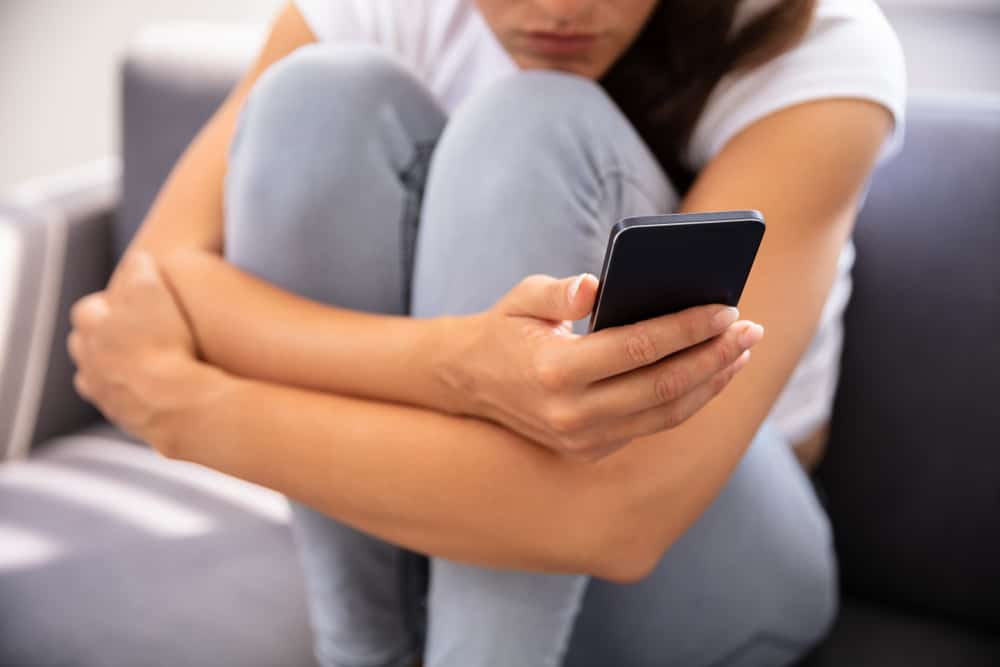 Eine junge Frau sitzt zusammengerollt auf einem Sofa und benutzt ein Handy