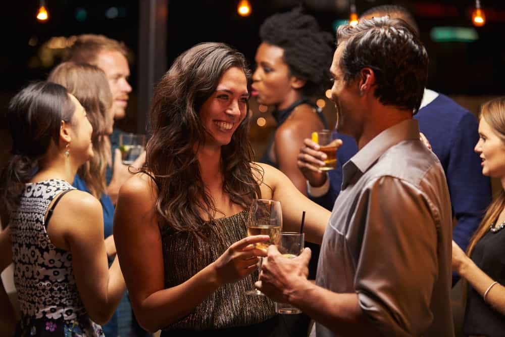 Eine lächelnde Frau auf einer Party tanzt mit einem Mann und trinkt Wein
