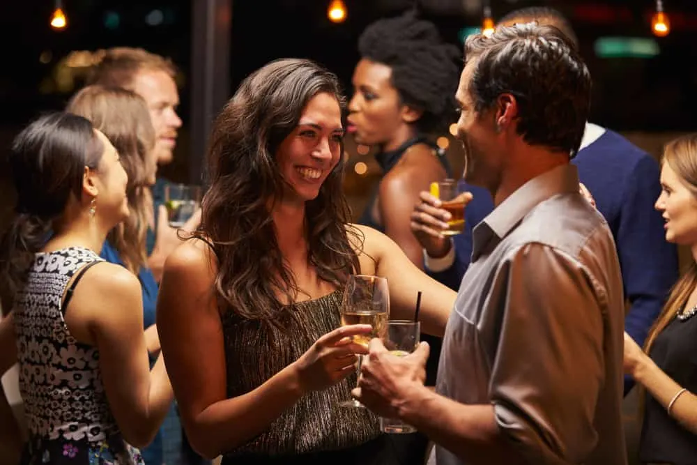 Eine lächelnde Frau auf einer Party tanzt mit einem Mann und trinkt Wein