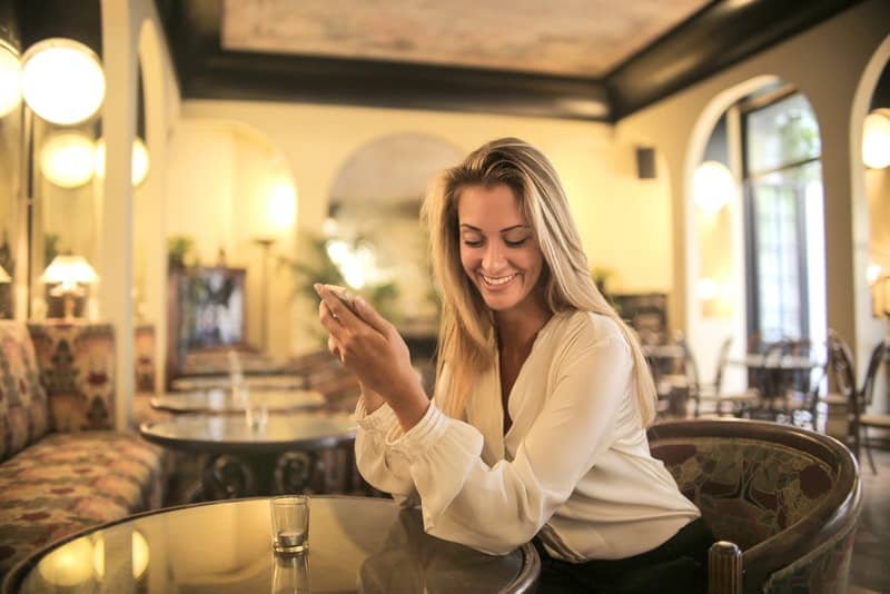 Eine lächelnde Frau trinkt in einem Café und benutzt ein Handy