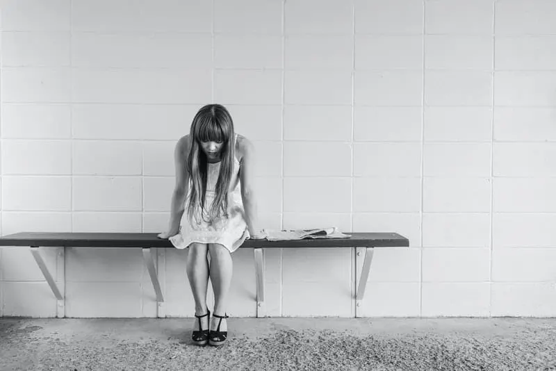Eine traurige Frau in einem weißen Kleid sitzt auf einer Bank