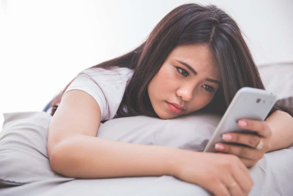 Eine traurige Frau liegt auf dem Bett und benutzt ein Smartphone