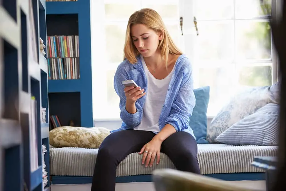 Eine traurige Frau mit einem Handy in der Hand sitzt auf der Couch im Haus
