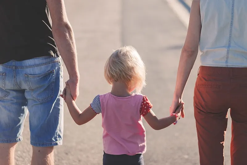Eltern halten Hände mit ihrem Kind, während sie auf der Straße gehen