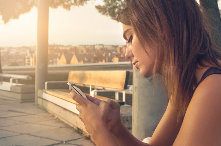 eine traurige Frau, die ein Smartphone betrachtet, während sie auf der Bank sitzt