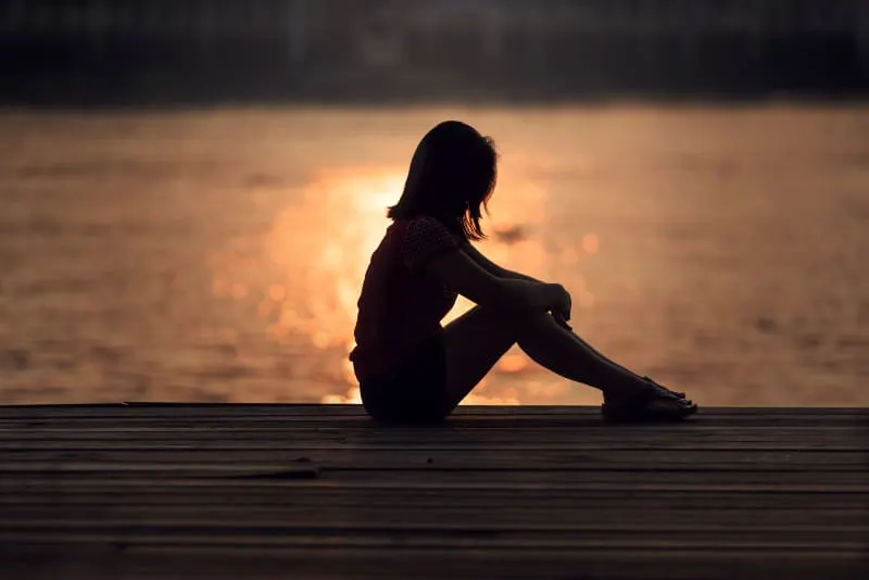 Silhouette einer Frau, die auf dem Dock bei Sonnenuntergang sitzt