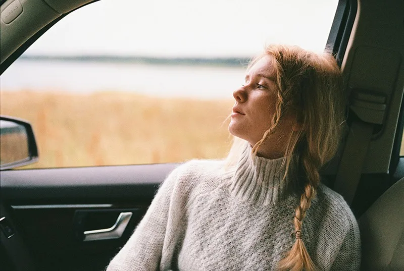 Frau im Pullover sitzt in einem Auto und schaut durch das Fenster