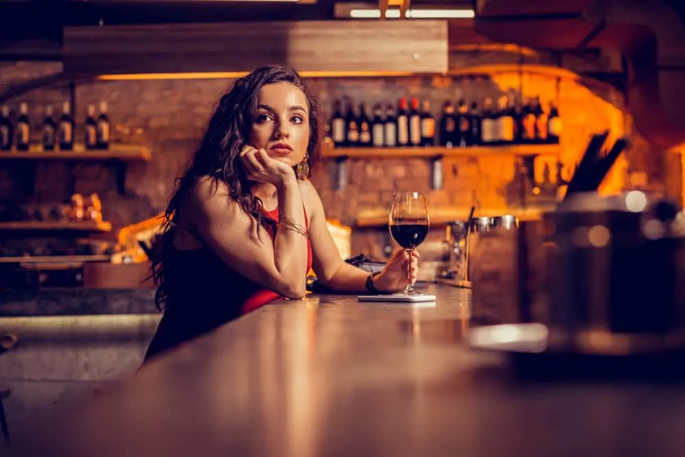 Hinter der Bar sitzt mit einem Glas Wein in der Hand eine nachdenkliche traurige Frau