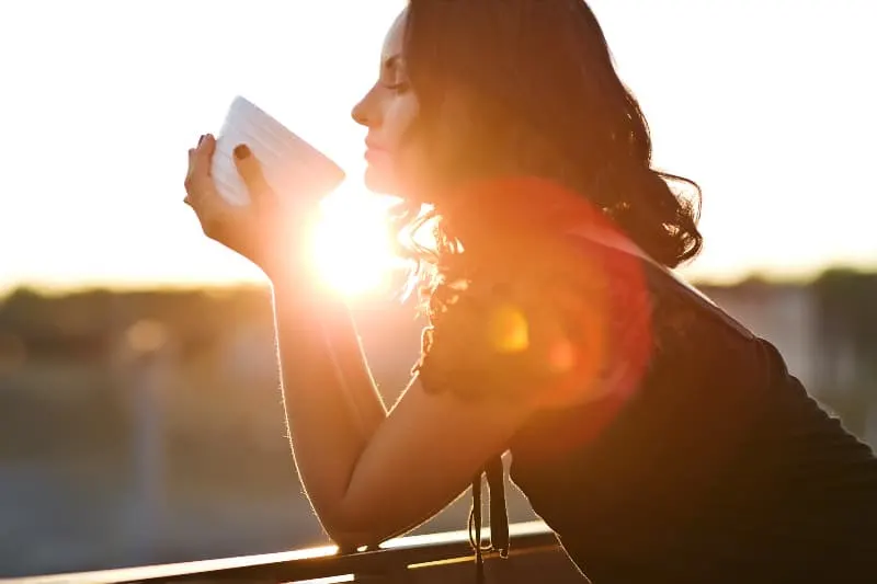 eine Frau, die Kaffee auf dem Balkon bei Sonnenuntergang trinkt