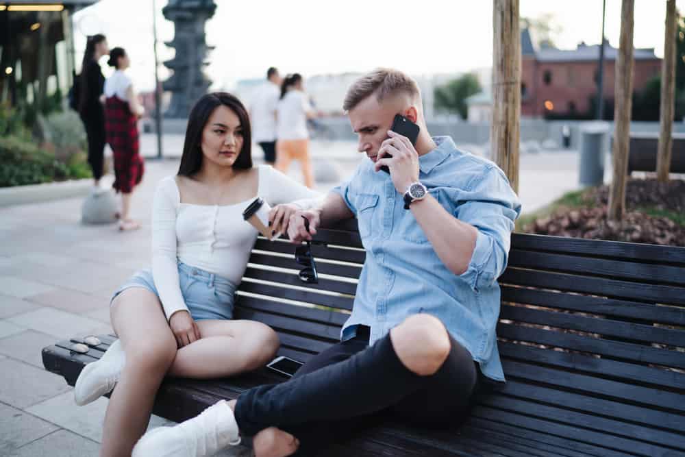 In der Stadt sitzen auf einer Bank eine Frau und ein Mann, die auf einem Handy sprechen