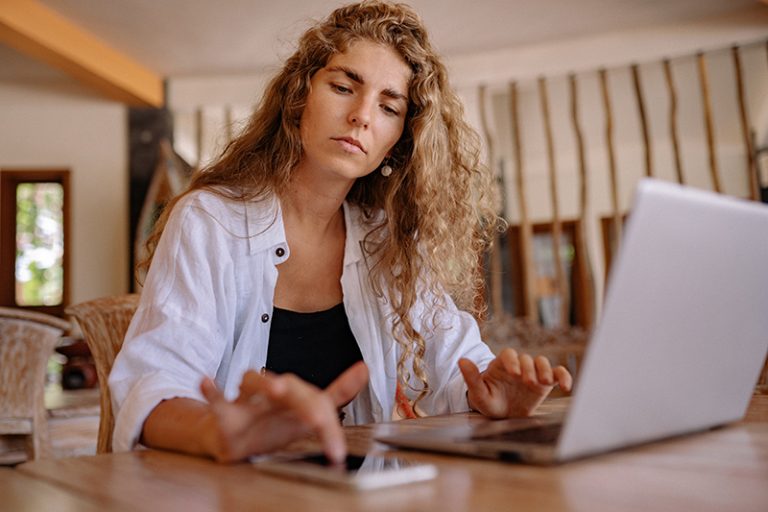 Eine besorgte Frau überprüft ihr Telefon, während sie vor dem Laptop sitzt