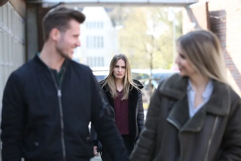 verärgerte Frau, die einen Ex-Freund und eine andere Frau ansieht, während sie hinter ihnen geht