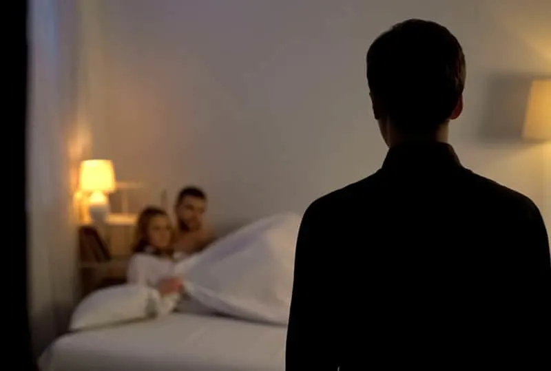 Mann, der seine Frau mit Liebhaber im Bett betrachtet, während er an der Tür steht
