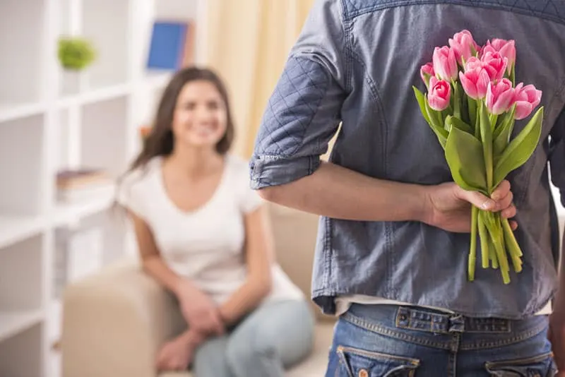 Mann hält Blumen als Überraschung für seine Frau