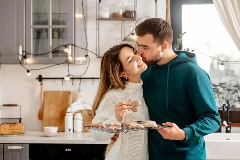 Mann küsst Frau in Wange, während Kekse halten