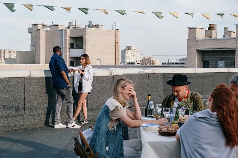 Mann und Frau flirten, während sie getrennt von Freunden auf einer Party auf einem Dach stehen
