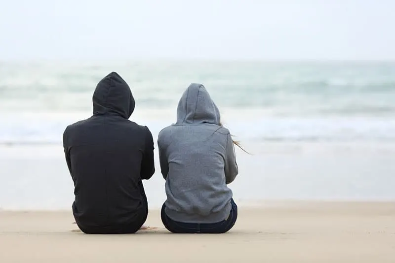 Paar in Kapuzenpullis am Strand sitzen