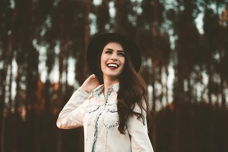 lächelnde Frau mit Hut im Park stehend