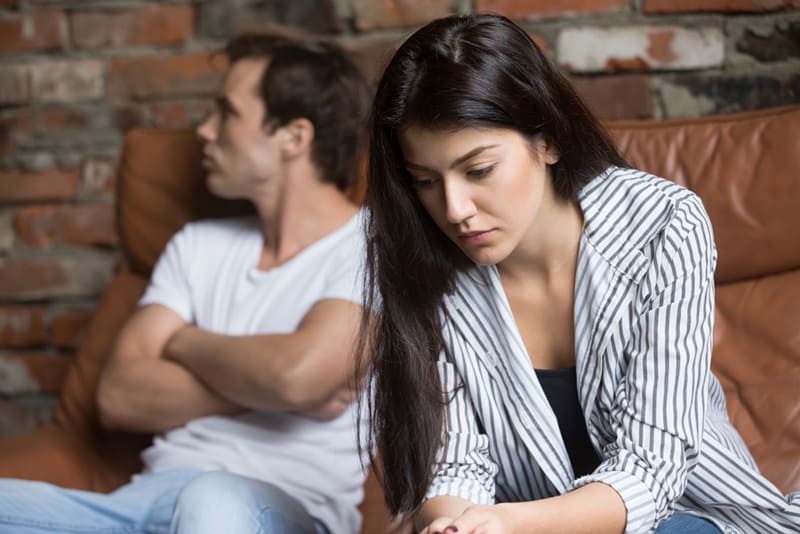 Traurige Frau, die an Beziehungsprobleme denkt, während ihr beleidigter Freund hinter ihr sitzt