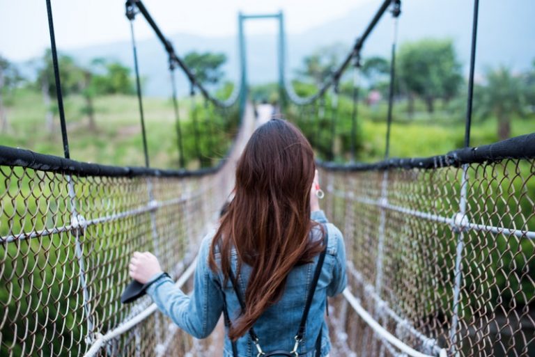 Eine Brünette in Jeansjacke überquert eine Hängebrücke