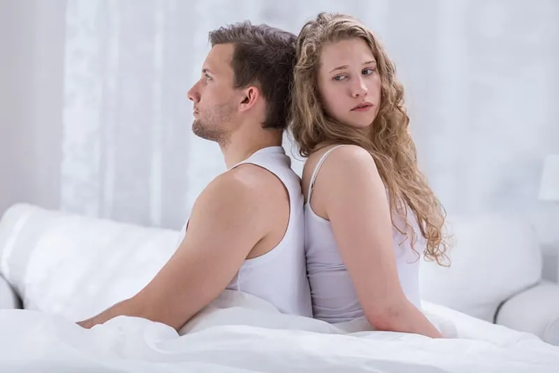 Ein Mann und eine Frau lehnen sich mit dem Rücken aneinander, während sie auf dem Bett sitzen