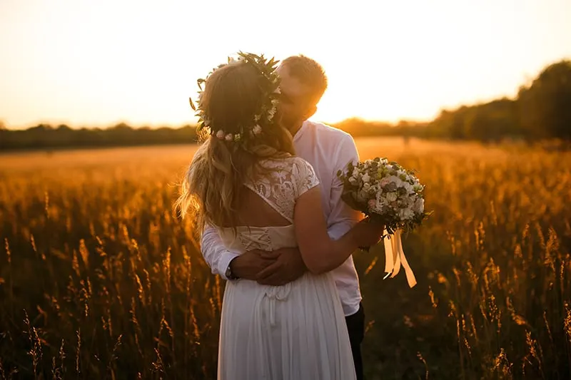 ein Hochzeitspaar, das sich küsst, während es während des Sonnenuntergangs auf dem Feld steht