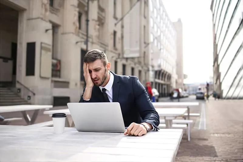 Ein Mann berührt das Gesicht mit der Handfläche, während er am Laptop arbeitet, und kann sich nicht auf die Arbeit konzentrieren