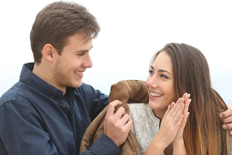 Ein Mann bedeckt eine Frau mit seiner Jacke bei kaltem Wetter und lächelt, während er sich ansieht