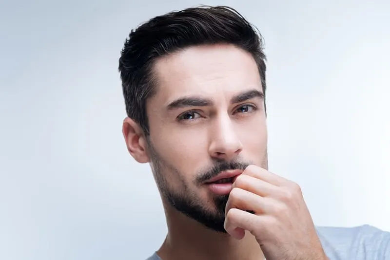 Ein Mann mit Bart berührt seine Lippen mit der Hand
