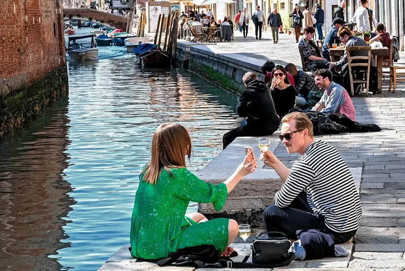 Ein Paar sitzt in der Nähe des Flusses in Venedig und trinkt Wein