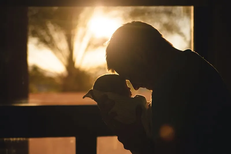 ein Vater, der ein Baby auf der Terrasse während des Sonnenuntergangs hält