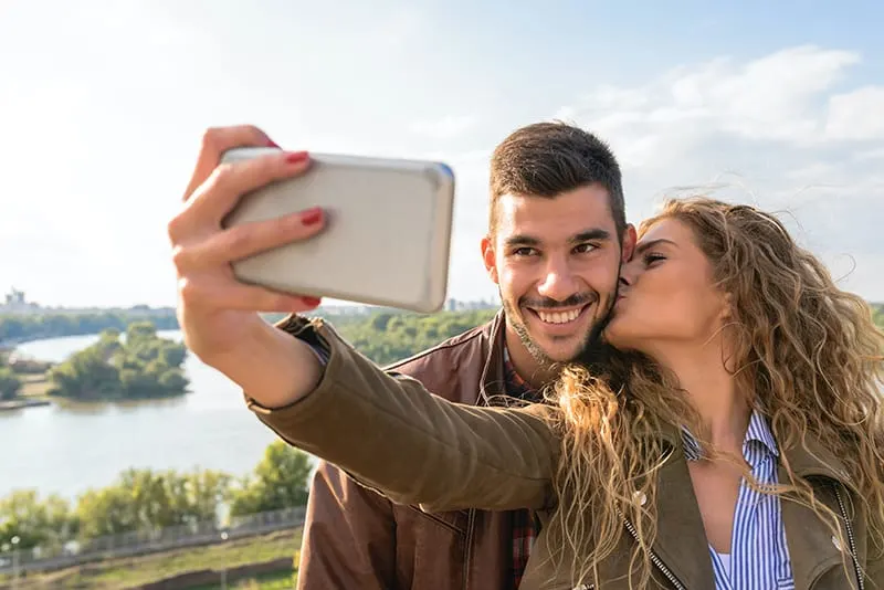 Ein glückliches Paar macht ein Selfie mit einem Smartphone, während es im Park steht