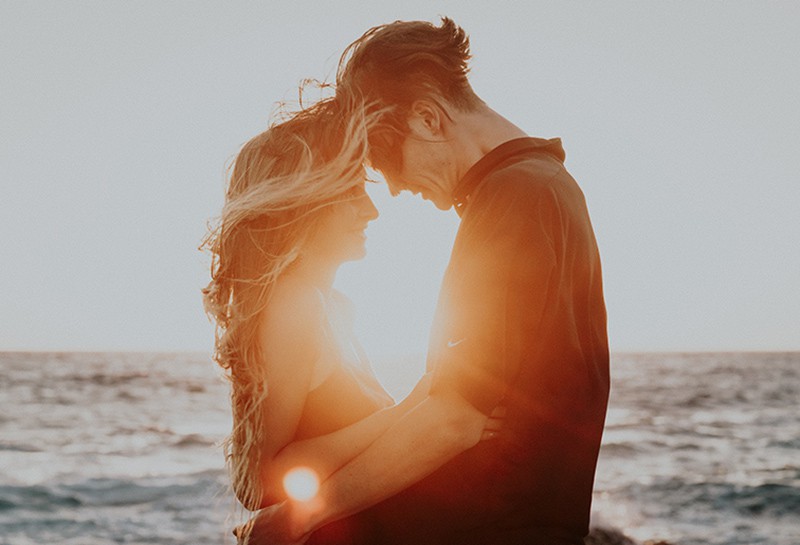 ein liebevolles Paar, das sich während des Sonnenuntergangs umarmt und ansieht