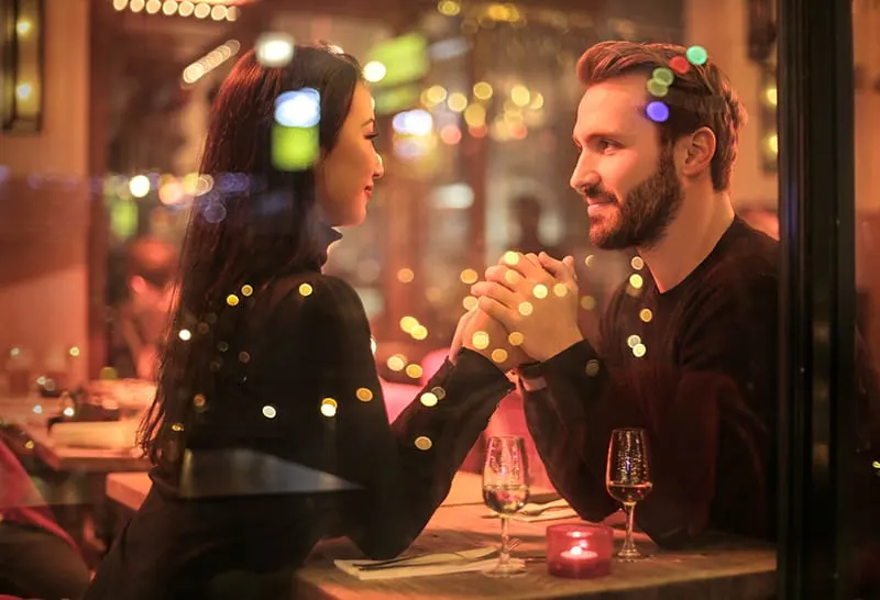 ein Paar Händchen haltend im romantischen Restaurant sitzend