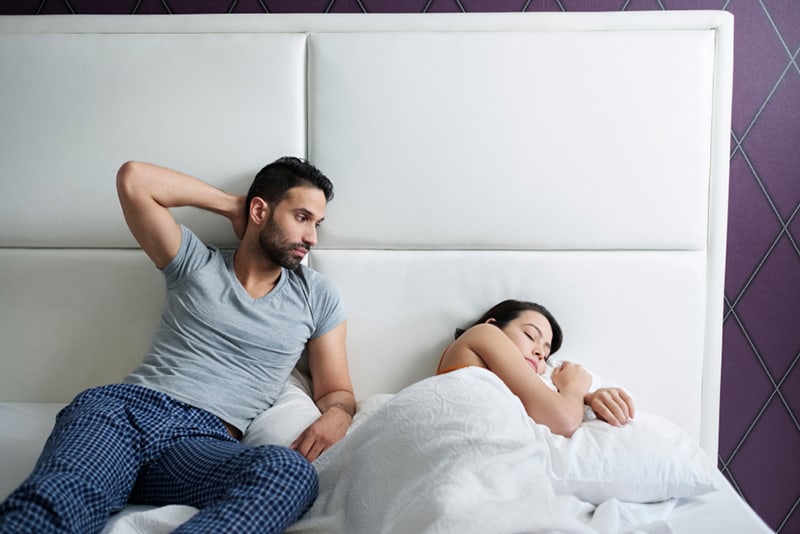 Ein trauriger Ehemann sieht seine Frau an, während sie im Bett schläft
