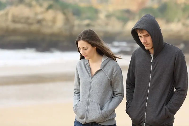 ein trauriges Paar, das zusammen am Strand spazieren geht