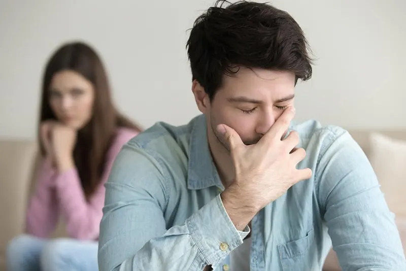 Ein verärgerter depressiver Mann, der den Mund mit der Handfläche bedeckt, während er vor seiner Freundin sitzt