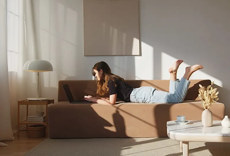 eine Frau, die auf der Couch liegt und einen Laptop benutzt, während sie sich in ihrer Wohnung entspannt