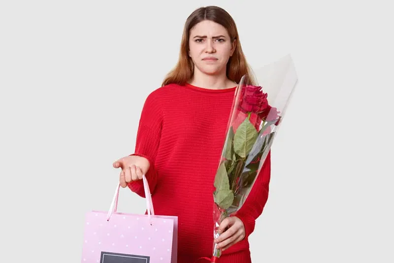 eine Frau mit einem Blumenstrauß und einer Geschenktüte, die unbefriedigt aussieht