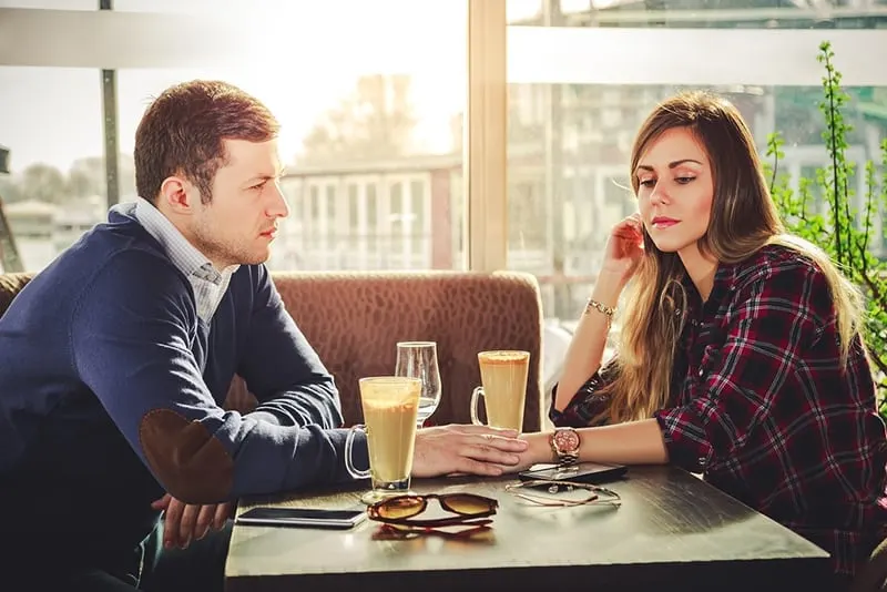 eine Frau, die nach unten schaut, während ihr Freund ihre Hand hält, während er zusammen im Café sitzt