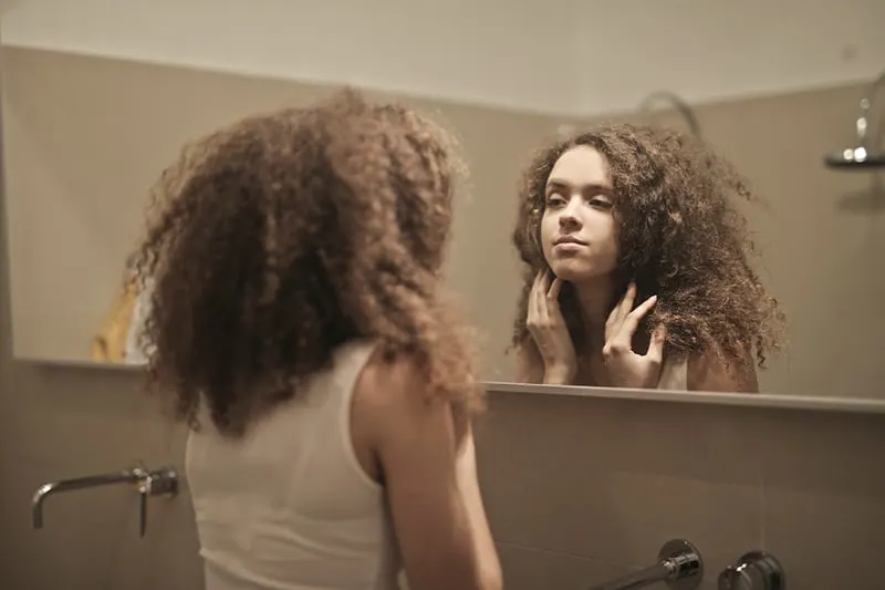 eine Frau, die sich in den Spiegel schaut und Haare mit den Händen berührt