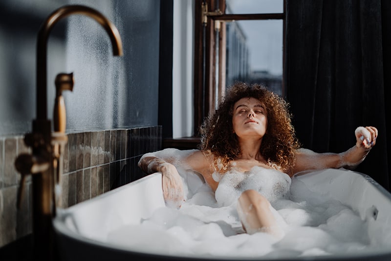 eine Frau, die sich in einem Bad mit geschlossenen Augen entspannt