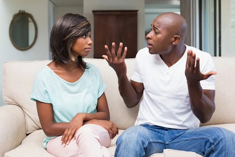 Eine Frau, die sich schuldig fühlt, hört einem Mann zu, der versucht, ihr etwas zu erklären, während er auf der Couch sitzt